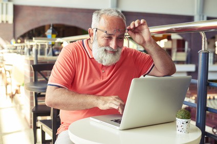 cheerful senior man raised his glasses cheerful senior man raised his glasses and looking at laptop in cafe