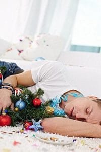 Drunk man sleeping on the floor embracing Christmas tree